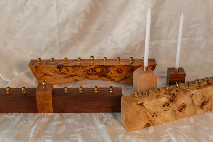 A group of handmade modern menorahs in walnut, maple, and mappa burl, shown with brass and copper candle cups