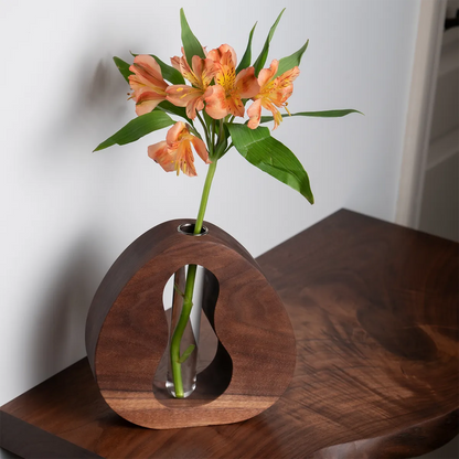Handcrafted walnut bud vase with sculptural cutout design and glass insert, holding orange blooms — a modern, minimalist gift for plant lovers.