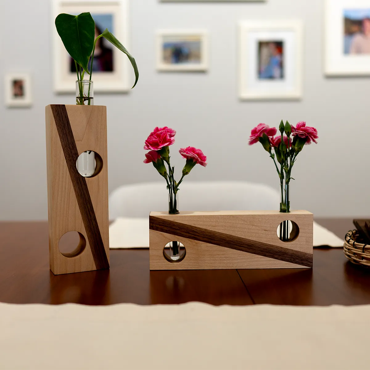 Handcrafted maple and walnut bud vases with modern geometric cutouts, holding pink carnations and greenery, a unique, handcrafted gift for plant lovers.