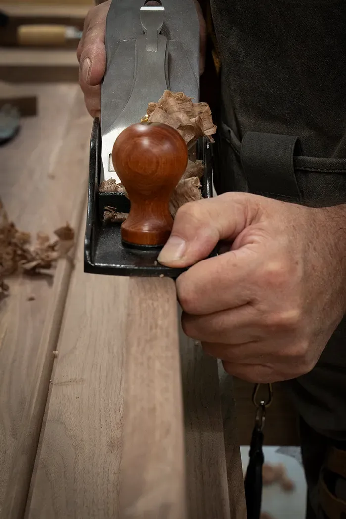 Close-up of a craftsman hand-planing a walnut board in a custom furniture workshop