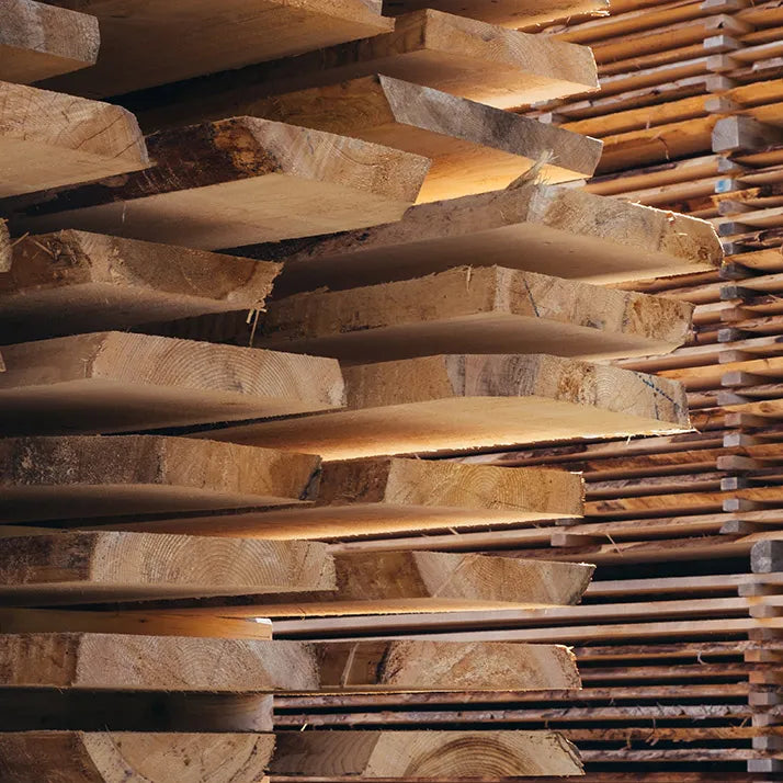 Stacks of rough-sawn hardwood boards in a woodshop, the first step in crafting custom furniture by hand.