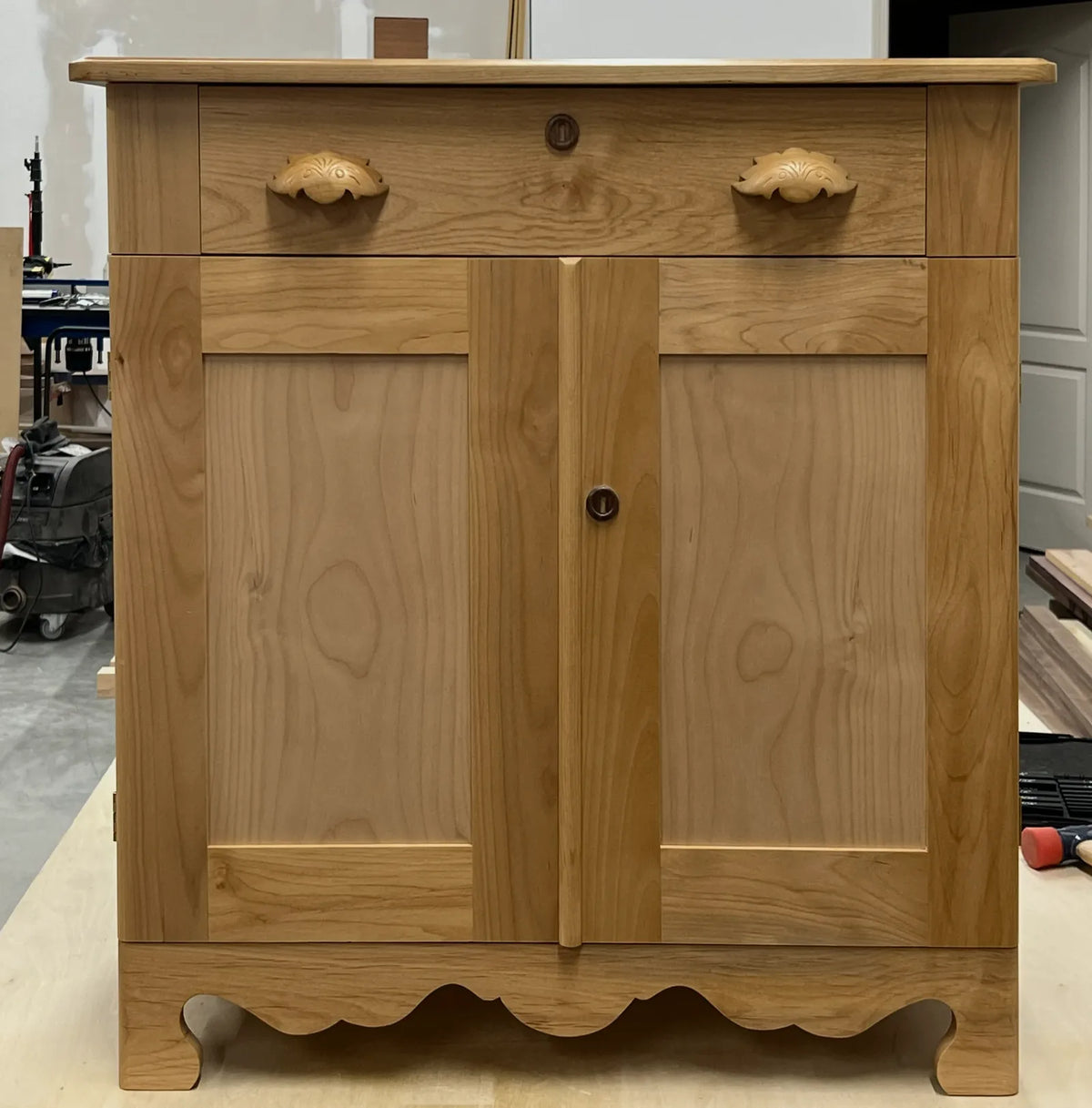 The finished alder washstand with carved bin pulls and a scalloped apron