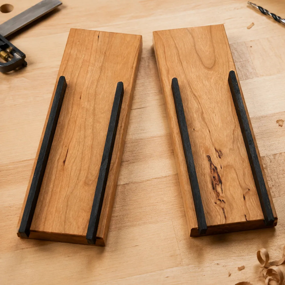 Cherry hardwood knife block components with ebony-dyed dividers on a maple workbench, showing how a handmade wooden knife block is assembled.