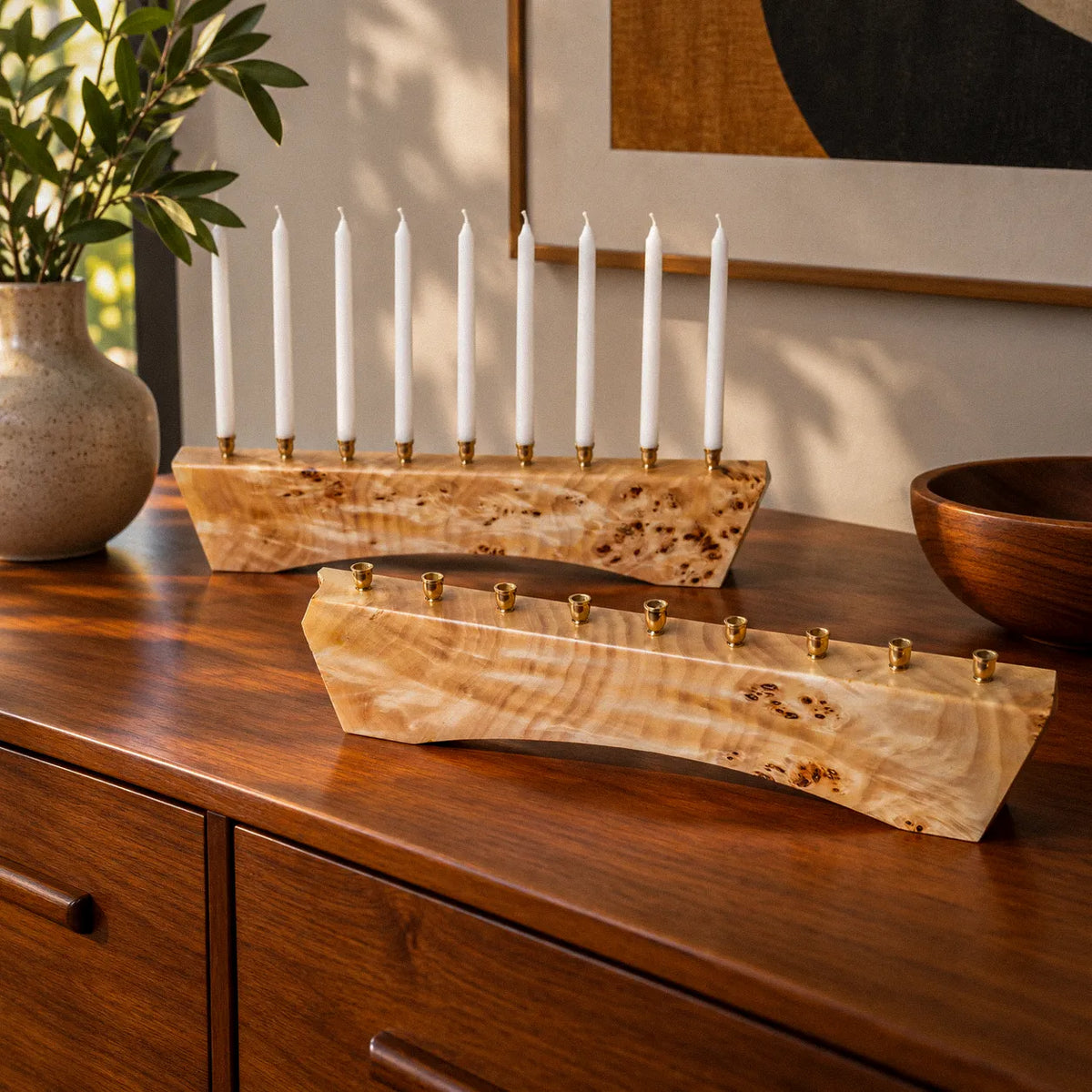 Two Hey Jude menorahs in solid Mappa burl, the front one showing the rippled chatoyant figure that shifts with the light, with brass candle cups