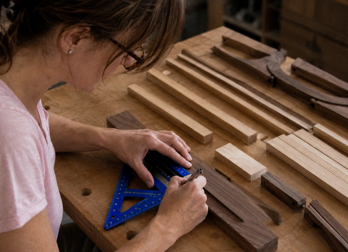 Asha marking a walnut board with a pencil against a speed square