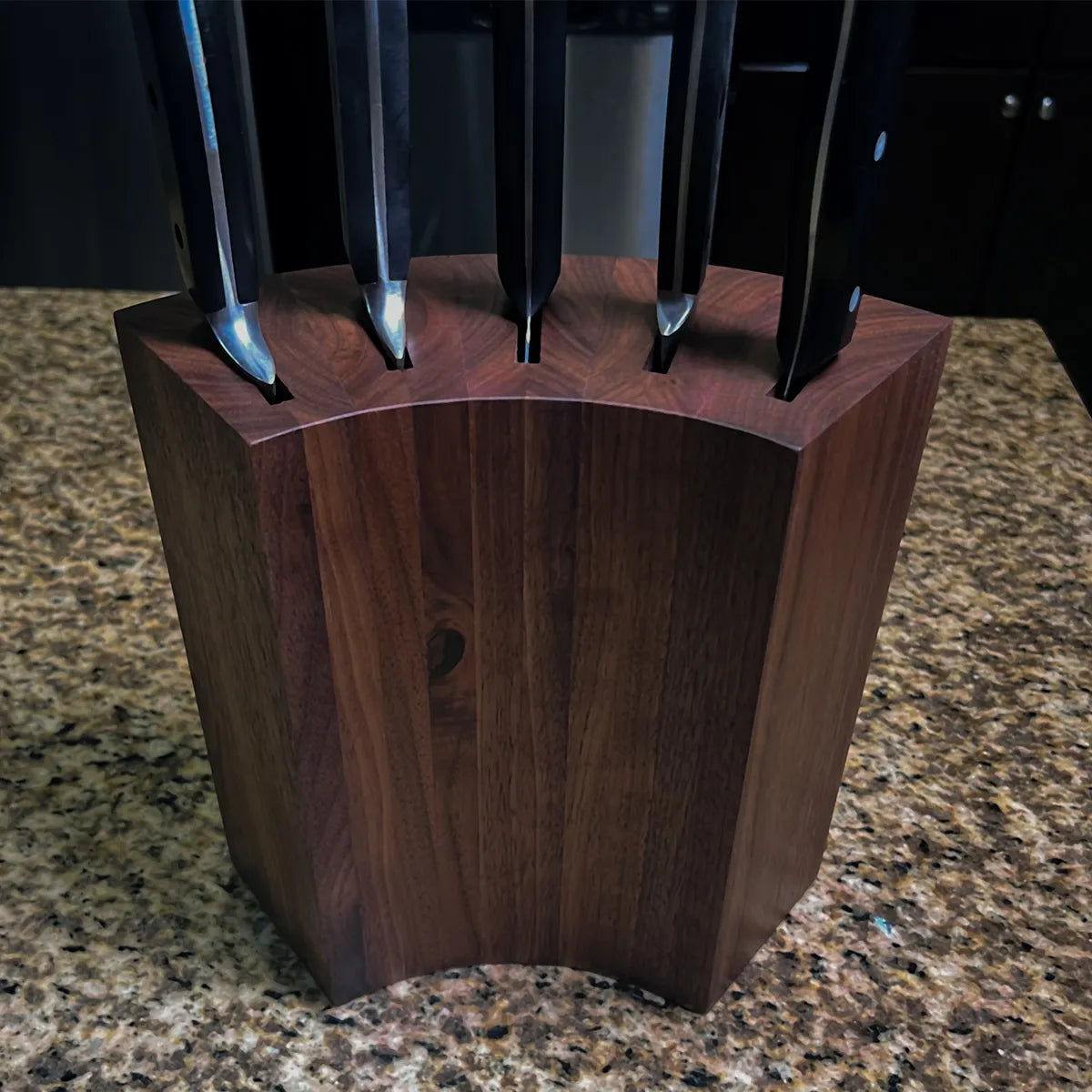 Minimalist walnut knife block with smooth curved back and stable countertop footprint.
