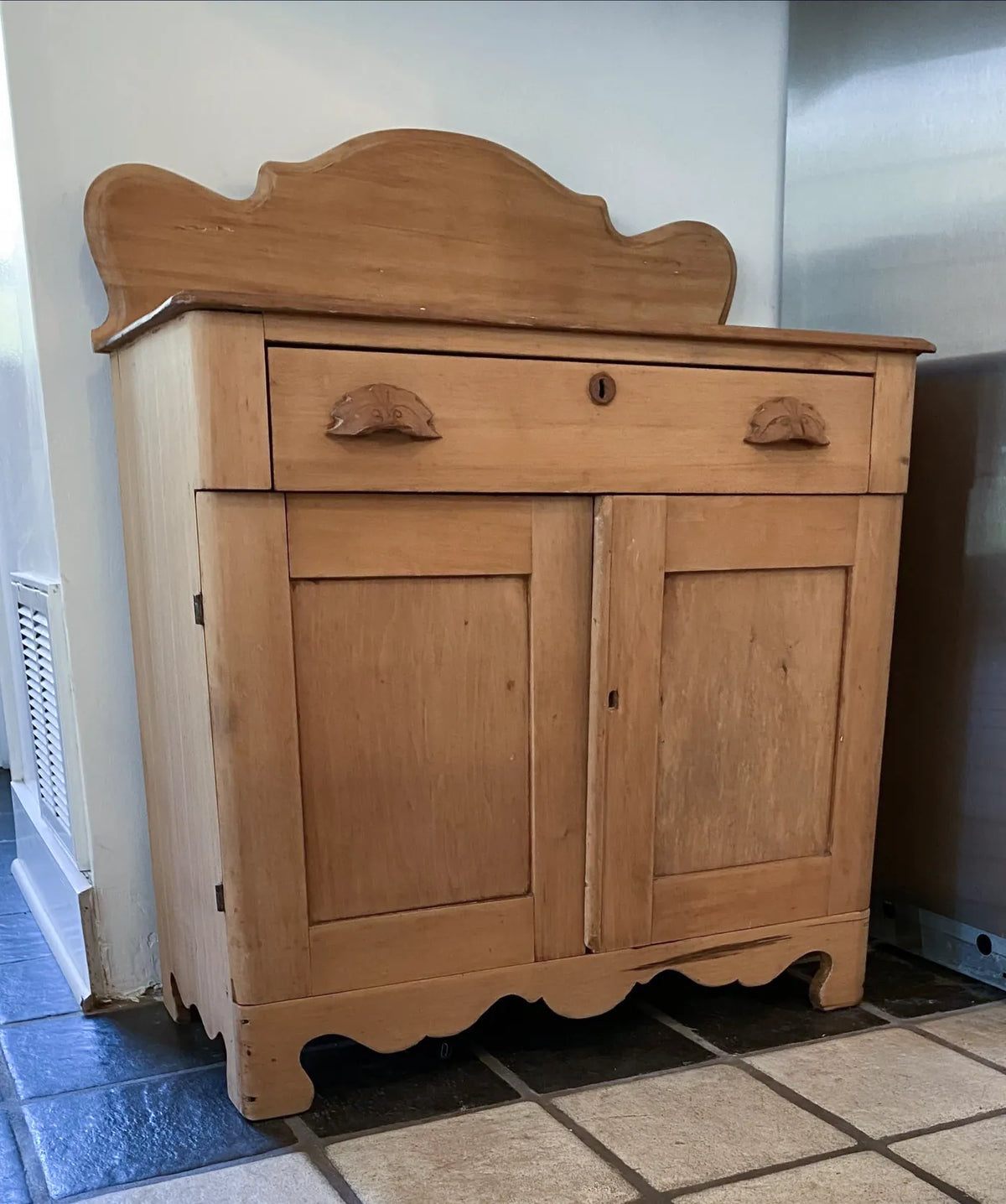 The original handmade washstand: a light wood cabinet with a scalloped backsplash and carved bin pulls