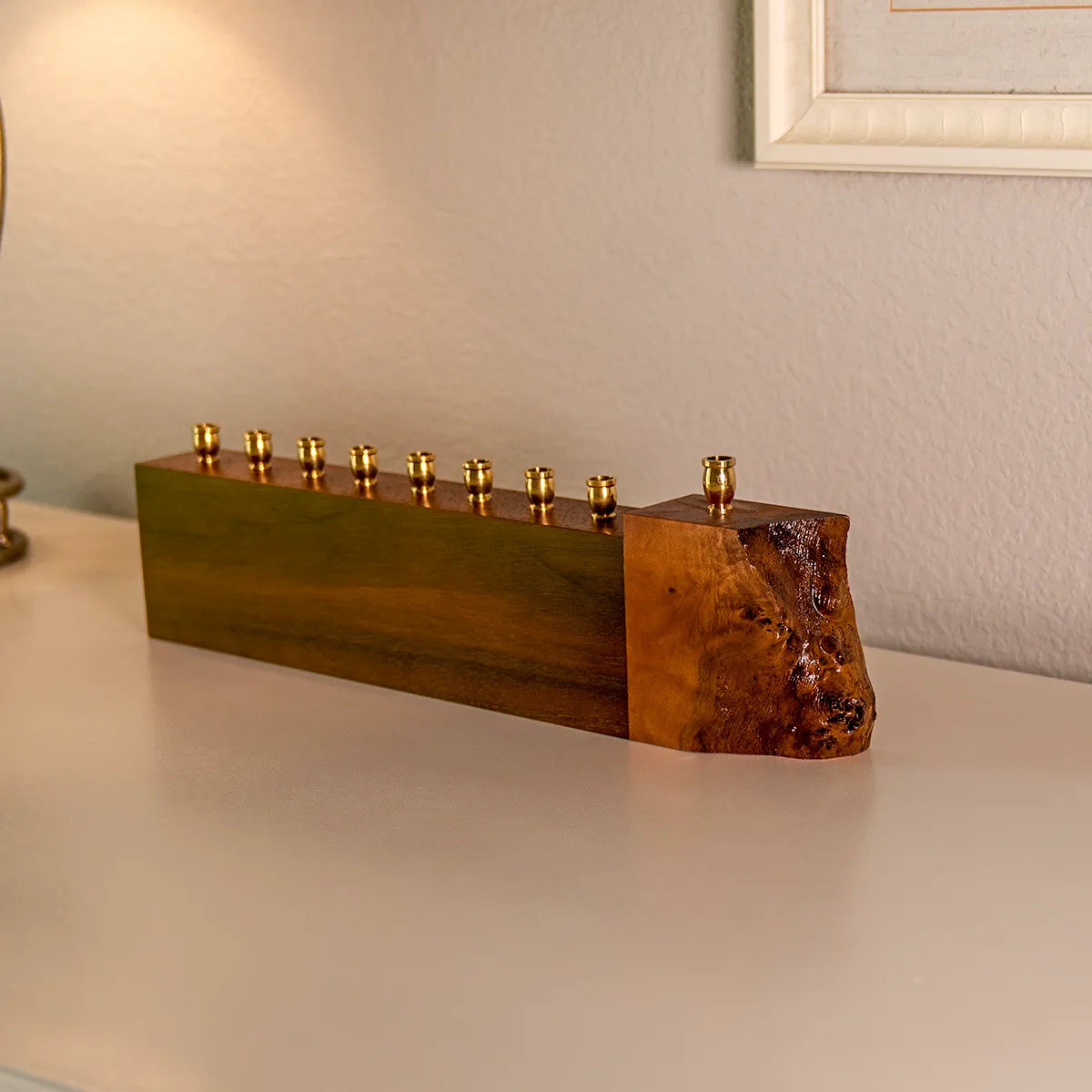 Angled view of a walnut and mappa burl menorah with brass candle cups on a white dresser