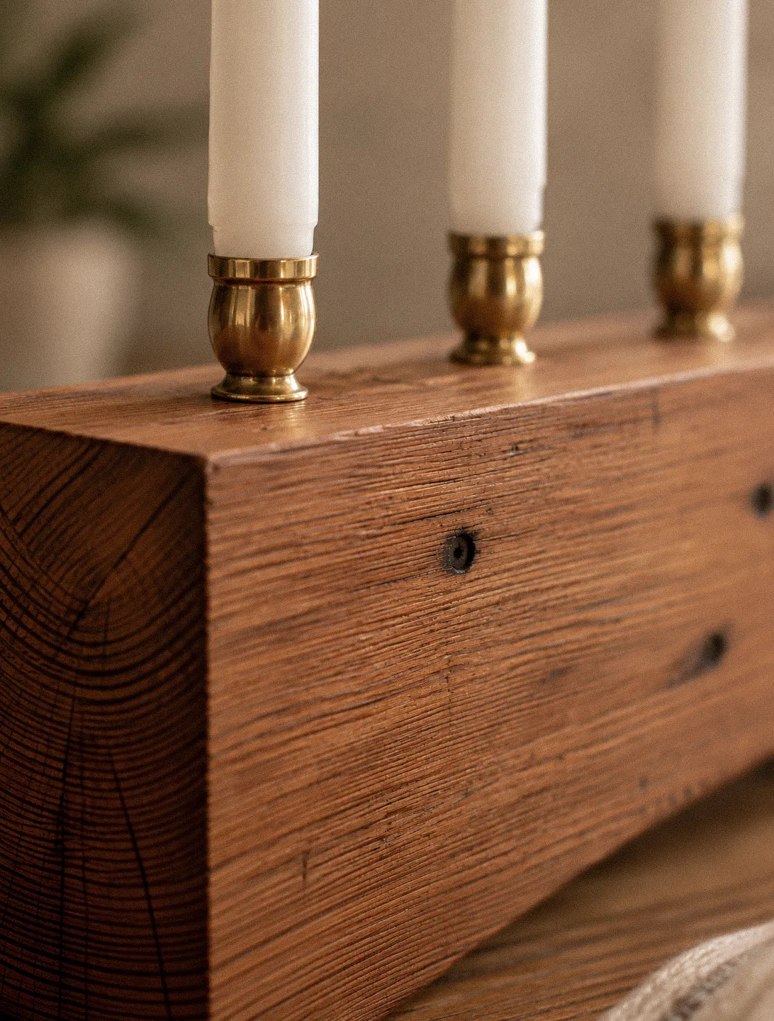Close detail of the 500 Miles menorah in reclaimed heart pine, showing dark nail holes preserved along the smooth, oil-finished face and the tight end grain at the corner.