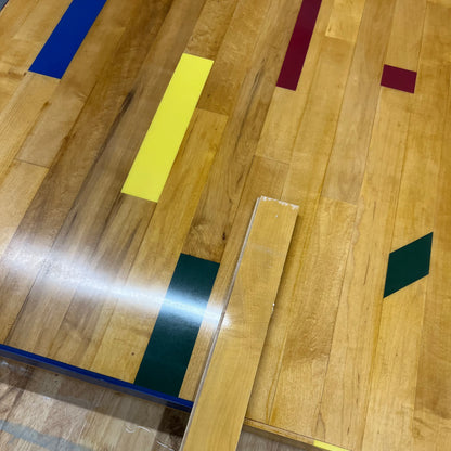 Close-up of reclaimed gym floor maple showing painted basketball court markings after refinishing and comparing the color to a piece of original floor
