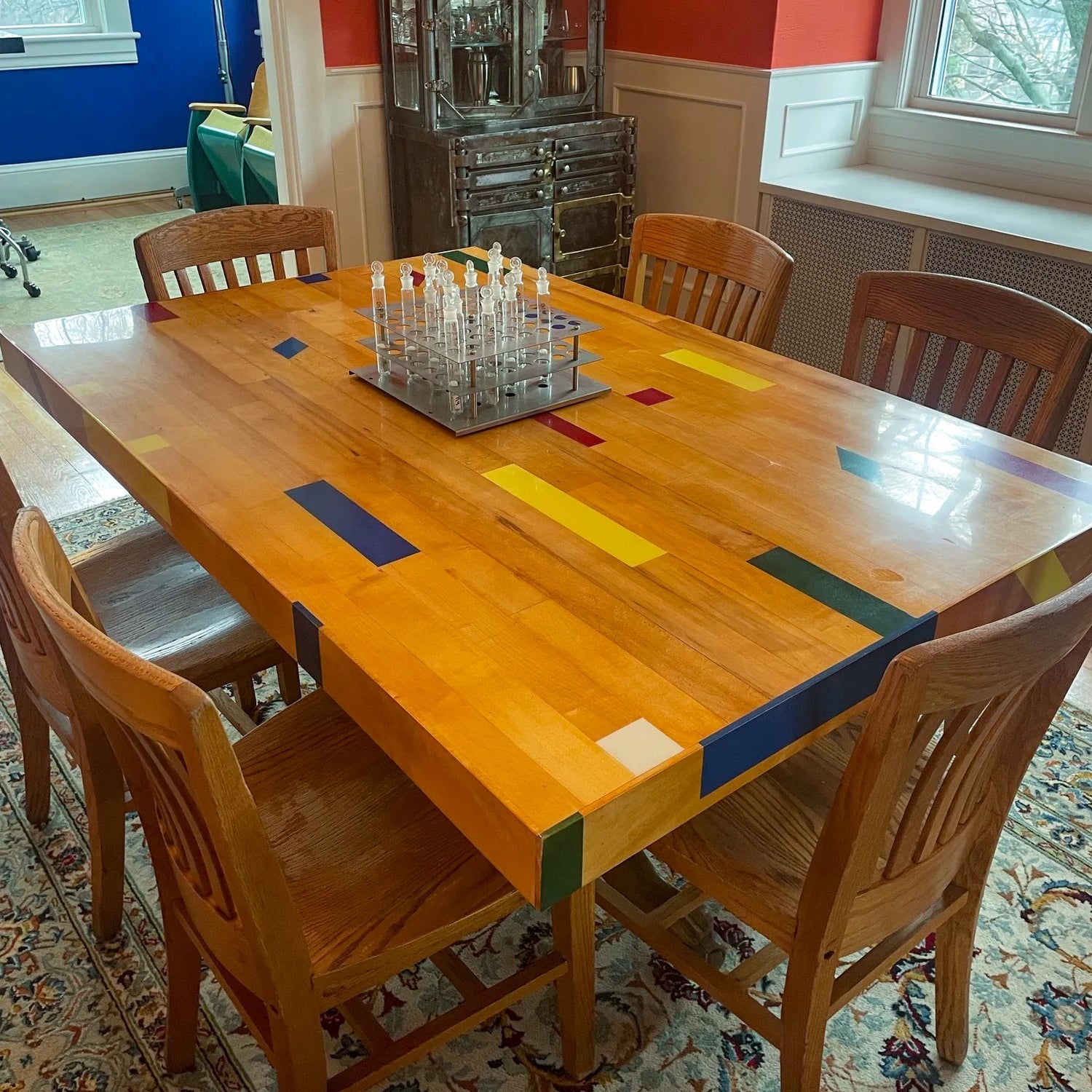 Reclaimed gym floor dining table made from refinished maple basketball court flooring with colorful inlay strips, shown in a dining room