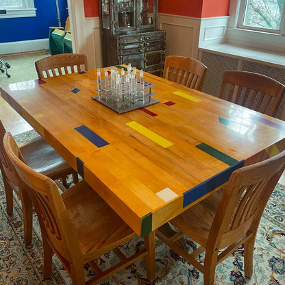 Reclaimed gym floor dining table made from refinished maple basketball court flooring with colorful inlay strips, shown in a dining room