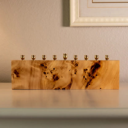 Solid mappa burl menorah with brass candle cups, handcrafted modern Hanukkah centerpiece displayed on a table.