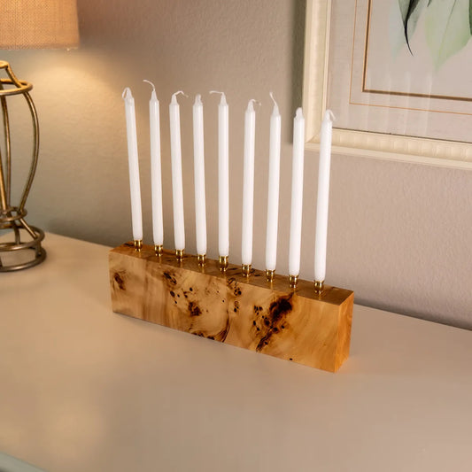 Solid mappa burl menorah with brass candle cups, displayed with white Hanukkah candles, highlighting the wood’s swirling grain and handcrafted quality.