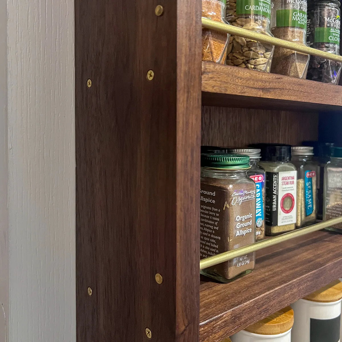 Close-up of a solid brass gallery rail and exposed brass screw on a walnut spice rack