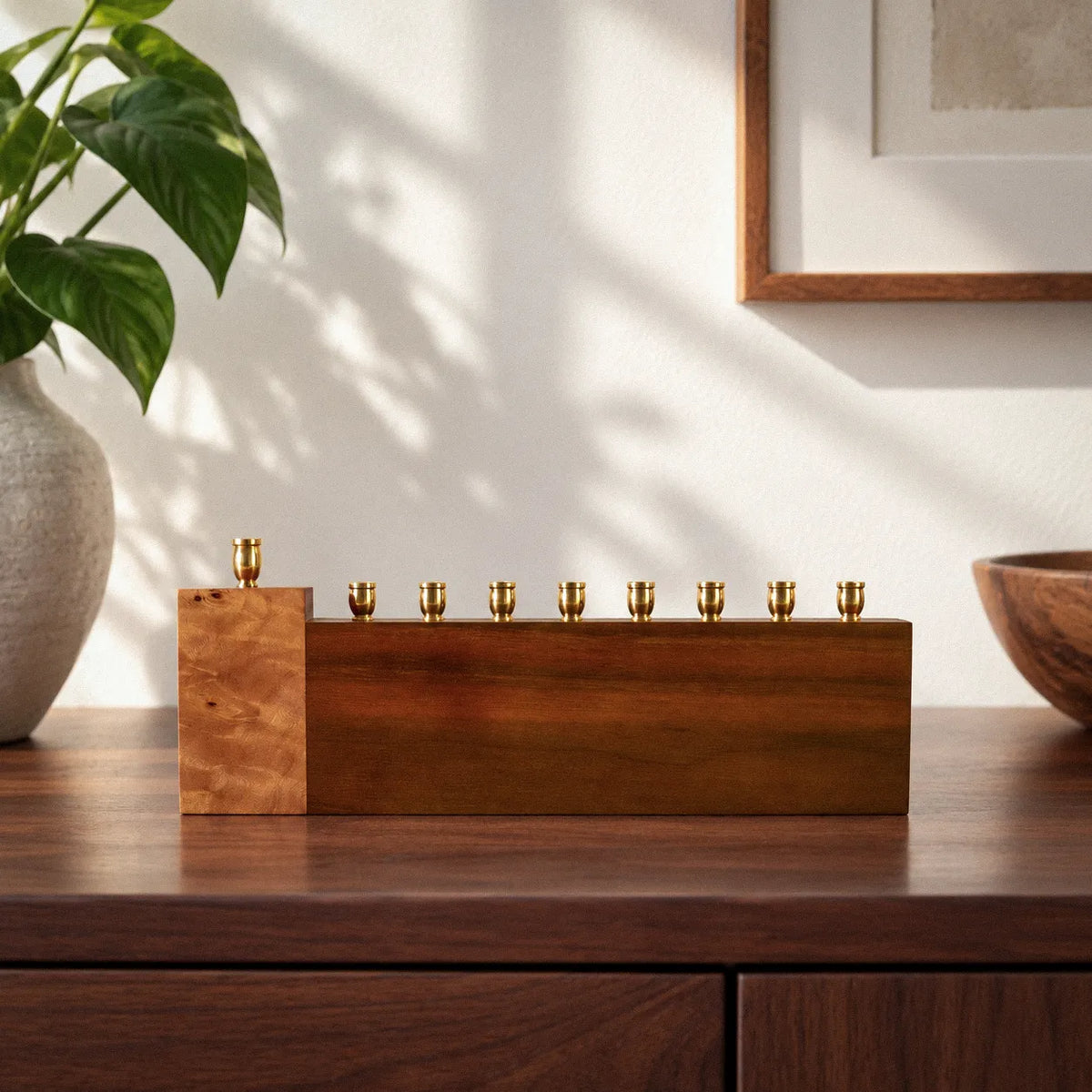 Piece of My Heart handmade Hanukkah menorah in solid walnut with a raised Mappa burl shamash block and eight brass candle cups, on a wood sideboard