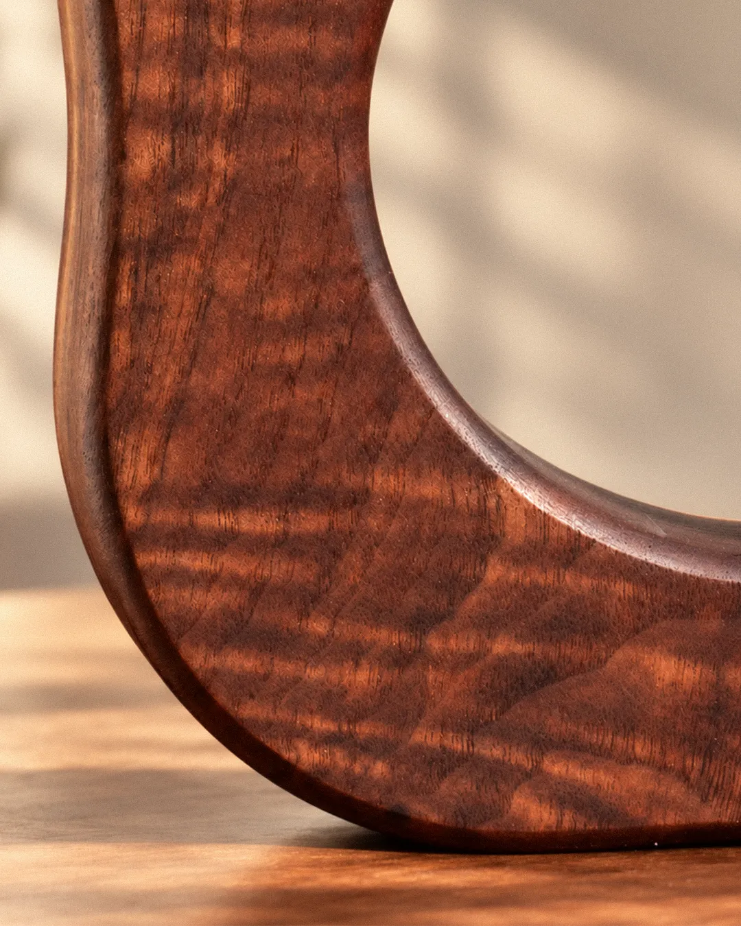 Close-up of a handmade walnut propagation vase showing curly grain detail and a half-visible round-bottom glass tube against a warm neutral background.
