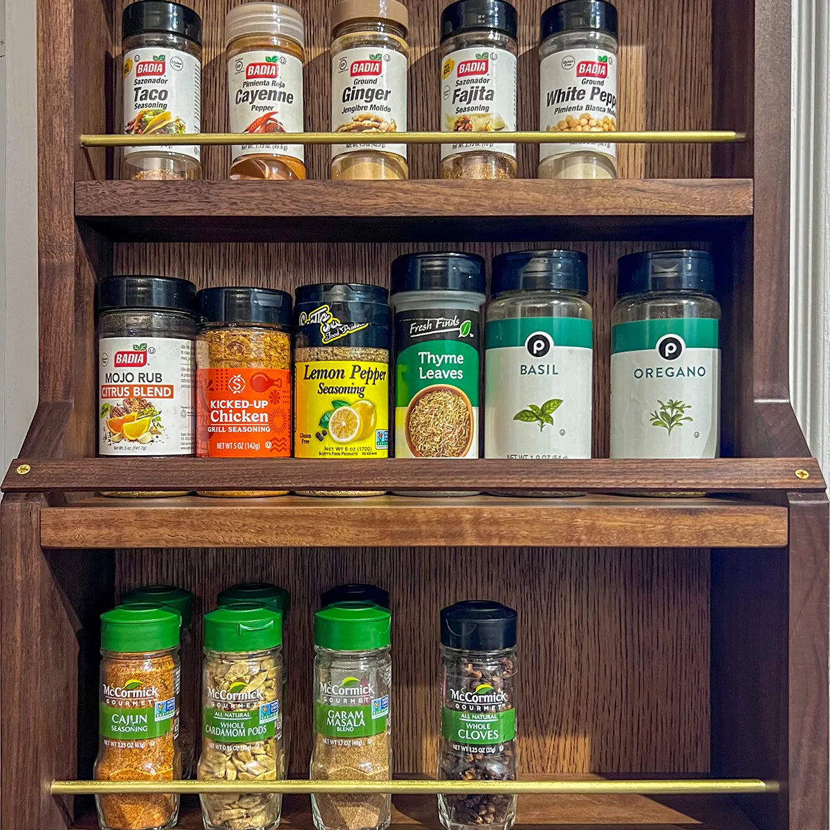Close-up of A Taste of Honey walnut spice rack filled with spice jars, showing solid brass retaining rails and walnut shelving.