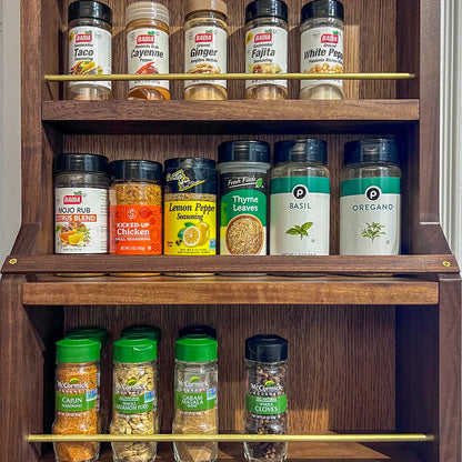 Close-up of A Taste of Honey walnut spice rack filled with spice jars, showing solid brass retaining rails and walnut shelving.